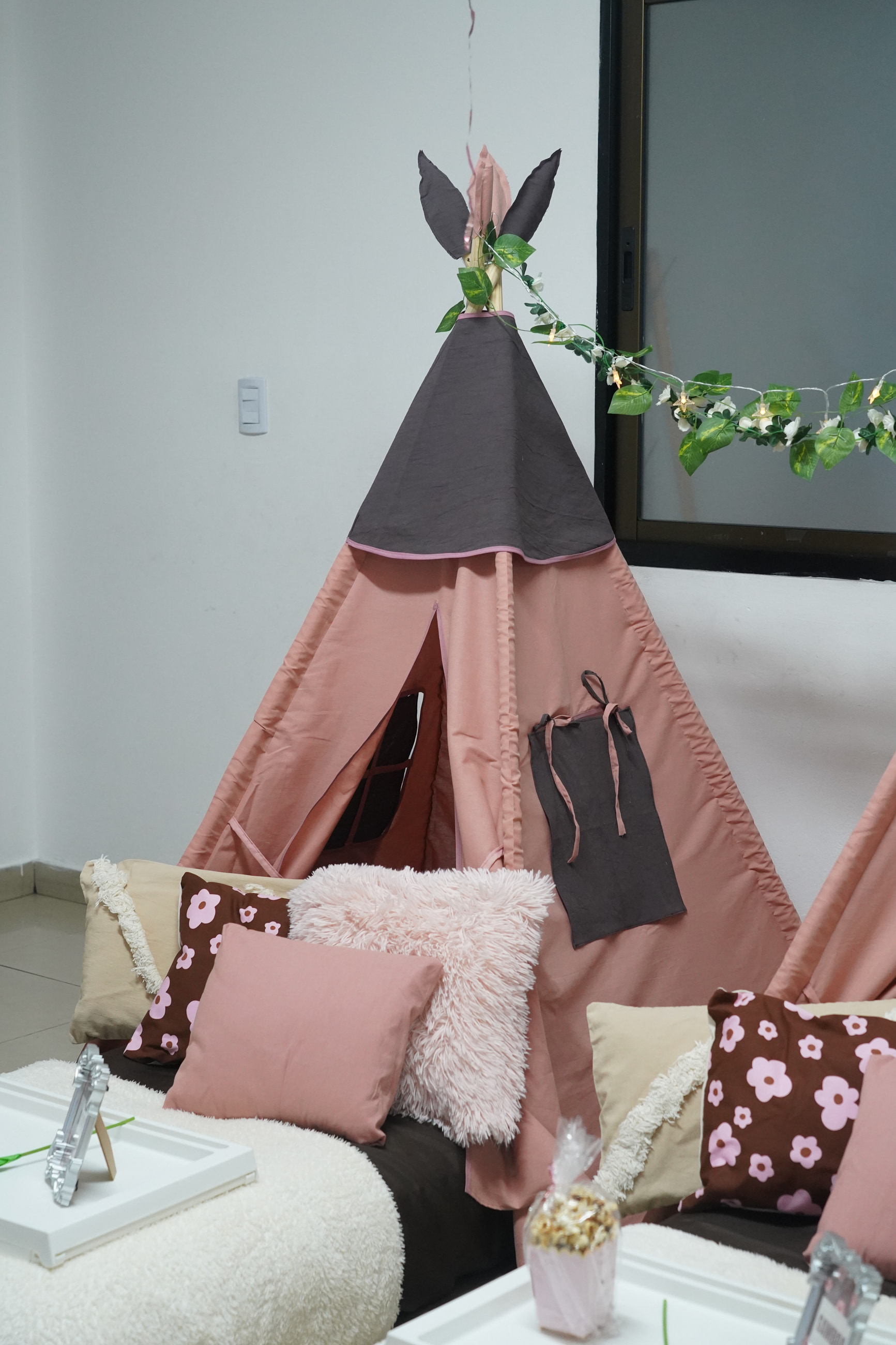 Una carpa tipi rosa con guirnalda de hojas y almohadones mullidos, floreados y lisos.