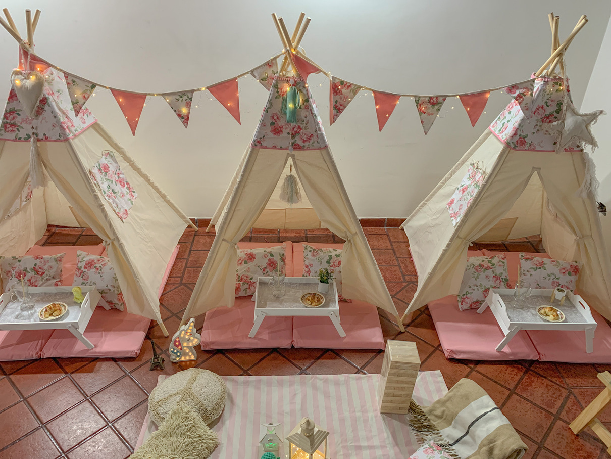 Tres carpas tipi crudas con colchonetas rosas, banderines de colores, almohadones floreados y bandejas blancas.