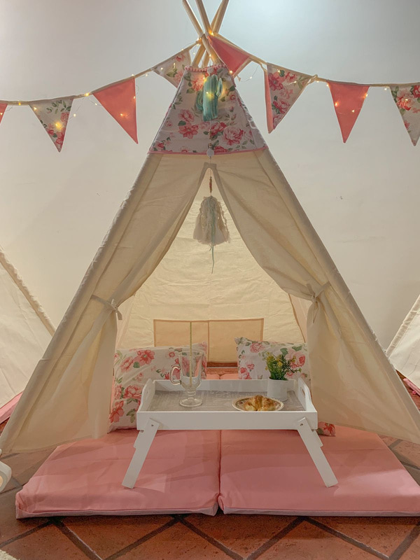 Una carpa tipi con colchoneta rosa, almohadones floreados y una bandeja con pata para el desayuno.